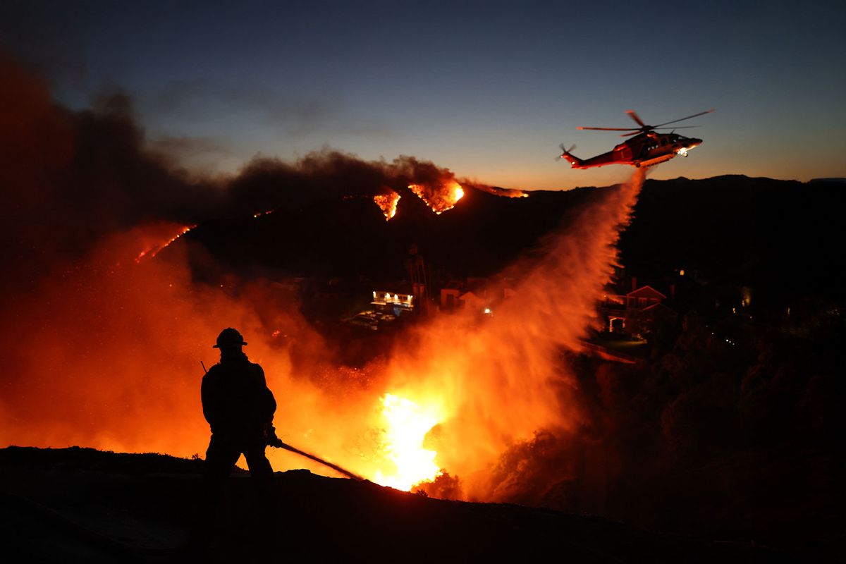 Fire personnel respond to homes destroyed while a helicopter drops water as the Palisades Fire grows in Pacific Palisades, California on January 7, 2025. (DAVID SWANSON/AFP via Getty Images)