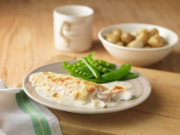 A plate of fish with peas and sauce.