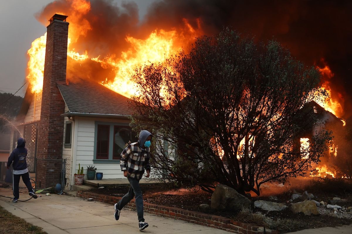 ALTADENA, CALIFORNIA - JANUARY 08: People attempt to save a neighboring home from catching fire during the Eaton Fire on January 8, 2025 in Altadena, California. Over 1,000 structures have burned, with two people dead, in wildfires fueled by intense Santa Ana Winds across L.A. County.  (Photo by Mario Tama/Getty Images)