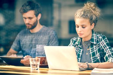 Young couple blogging on tablet an laptop inside cafe window