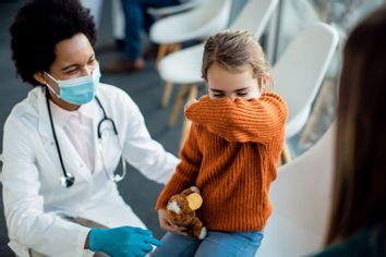 Little girl coughing into elbow while being at medical clinic