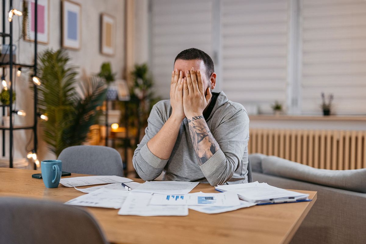 Stressed man covering his face with both hands and going through his bills and financial reports.
 (Getty Images/urbazon)