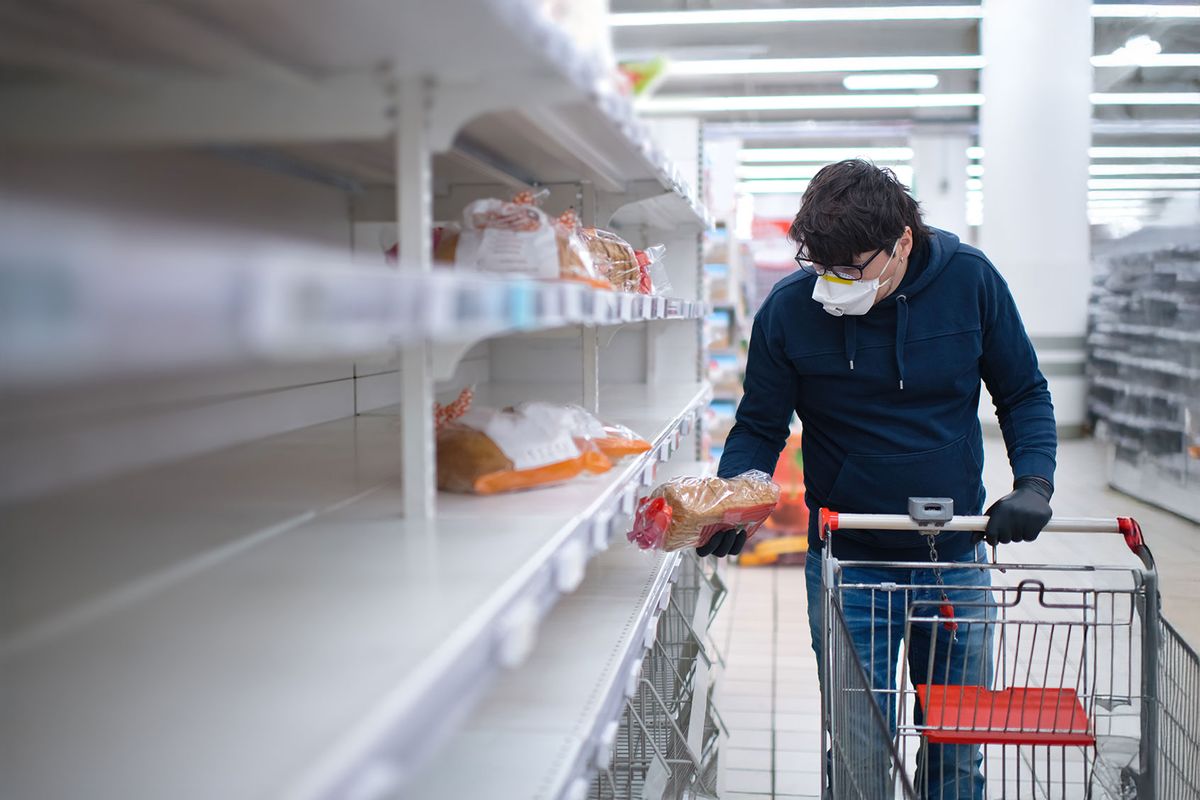 Man's hands in protective gloves searching bread on empty shelves in a groceries store (Getty Images/ArtMarie)