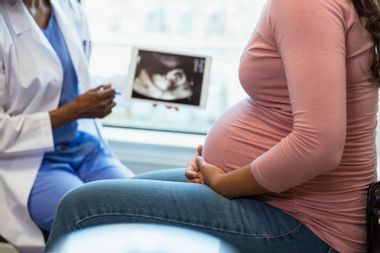 Pregnant woman in the foreground as the unrecognizable doctor shows her an ultrasound 