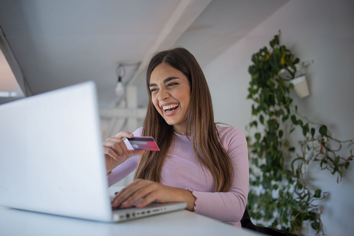 Woman happily holding credit card at computer, online shopping (Getty Images/Rockaa)