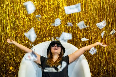 Woman lying in a bathtub with money raining down