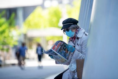 woman wearing a mask and gloves reads a local newspaper