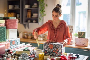 Woman wrapping gifts at home on the kitchen counter.