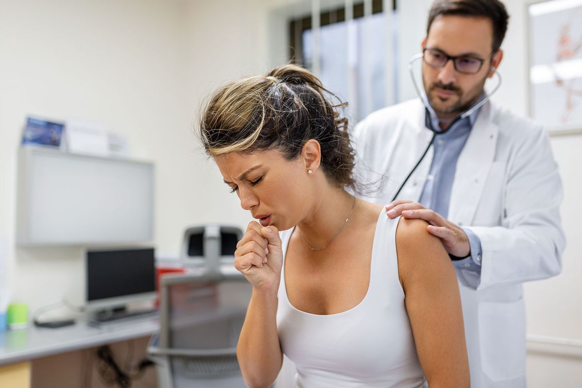 Young female patient in the clinic suffering a coughing fit while the doctor listens to the her lungs with a stethoscope. (Getty Images/stefanamer)