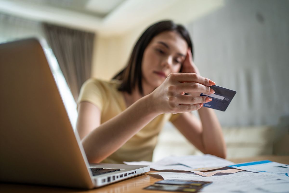 Young woman worried about finances, looking at credit card (Getty Images/Kiwis)