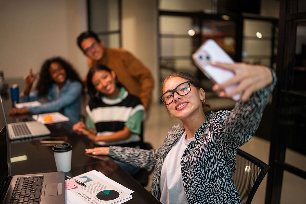 Young woman taking a selfie with coworkers at office (Getty Images/FG Trade Latin)